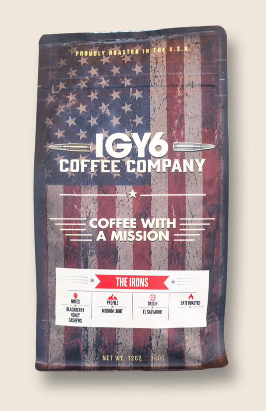 A stand-up coffee bag from IGY6 Coffee Company featuring a distressed American flag design in red, white, and blue, with the product name 'The Irons' shown on a white label near the bottom, photographed against a light beige background.